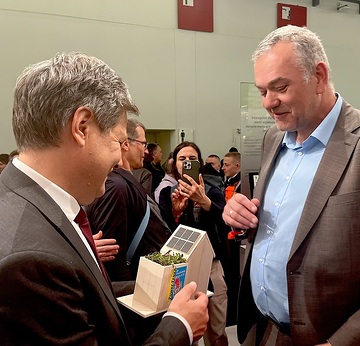 ZVDH-Präsident Dirk Bollwerk (rechts) übergibt Minister Habeck Holzhaus mit PV-Anlagen und Gründach, Bild: ZVDH